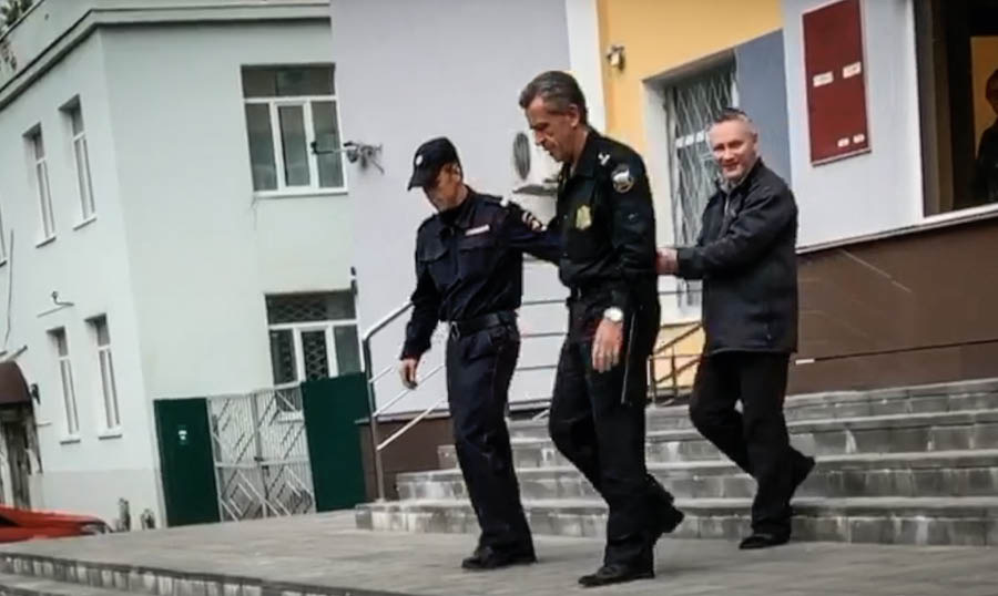 Aina no video ”Intervija ar brāli Dmitriju Mihailovu”. Divi policisti ved rokudzelžos saslēgto Dmitriju.