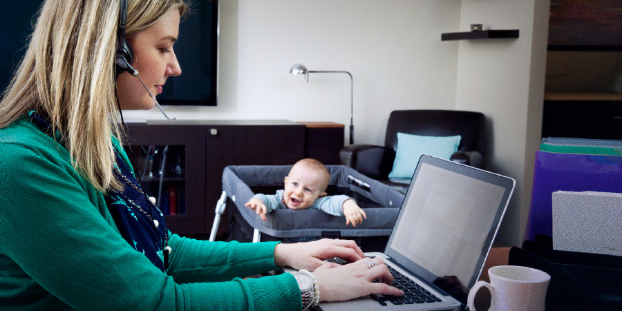 Een moeder die op haar computer aan het werk is terwijl haar baby om aandacht vraagt