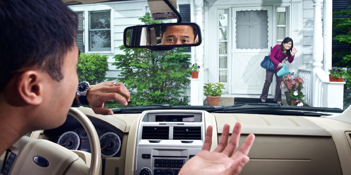 Een man in een auto die ongeduldig op zijn vrouw wacht terwijl zij de planten water aan het geven is