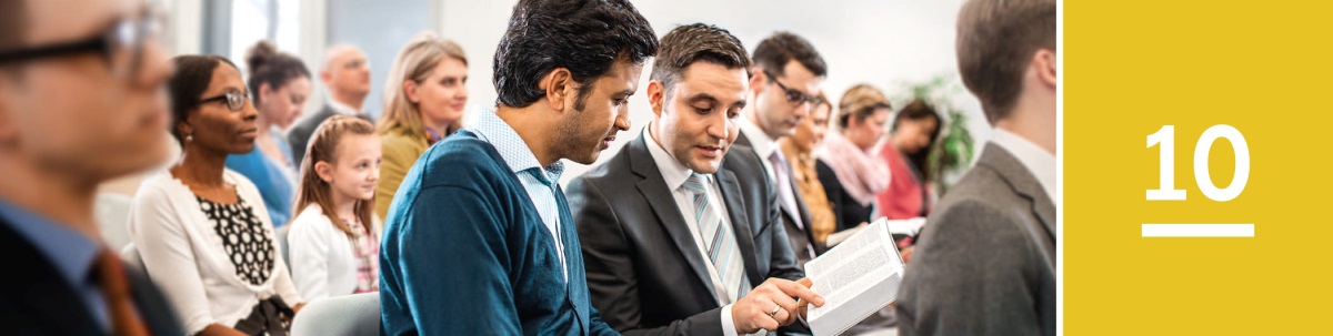 Les 10. Een man leest met een Getuige mee in de Bijbel tijdens een bijeenkomst van Jehovah’s Getuigen.