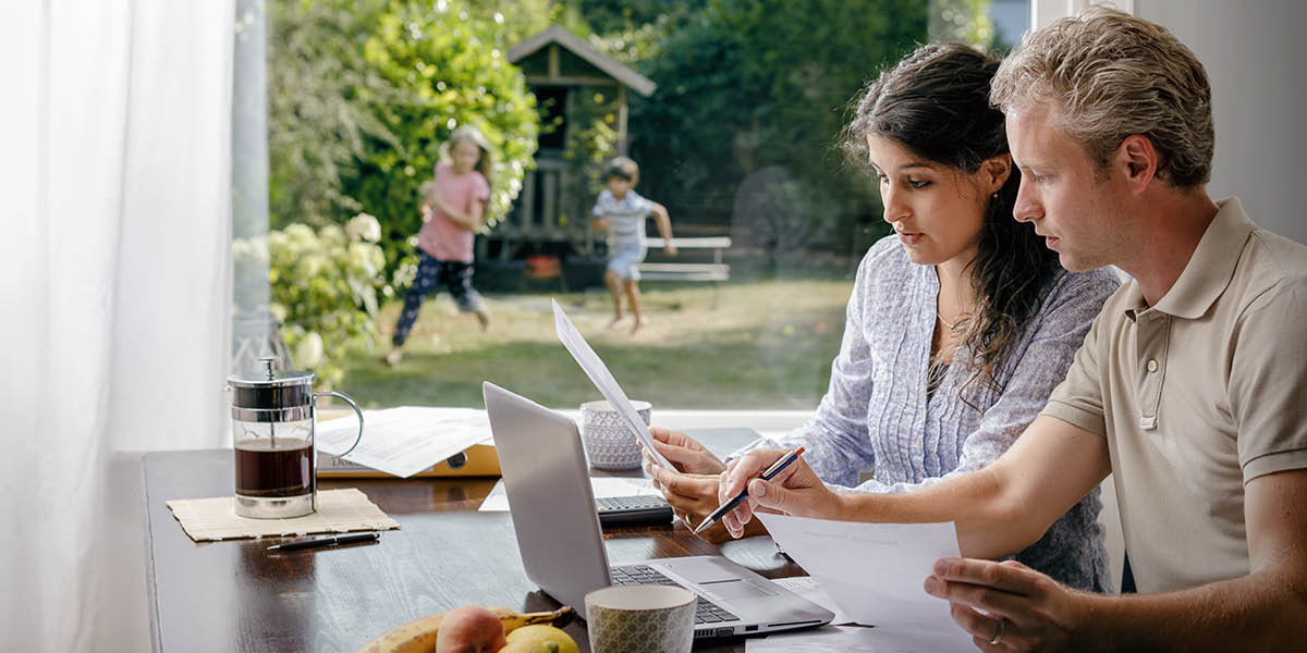 Ouders die hun financiën bespreken terwijl hun kinderen in de tuin aan het spelen zijn.