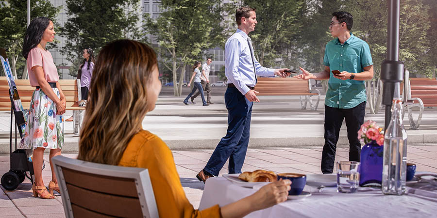 De broeder geeft de man zijn portemonnee terug, die hij was verloren, terwijl de vrouw op het terrasje toekijkt.