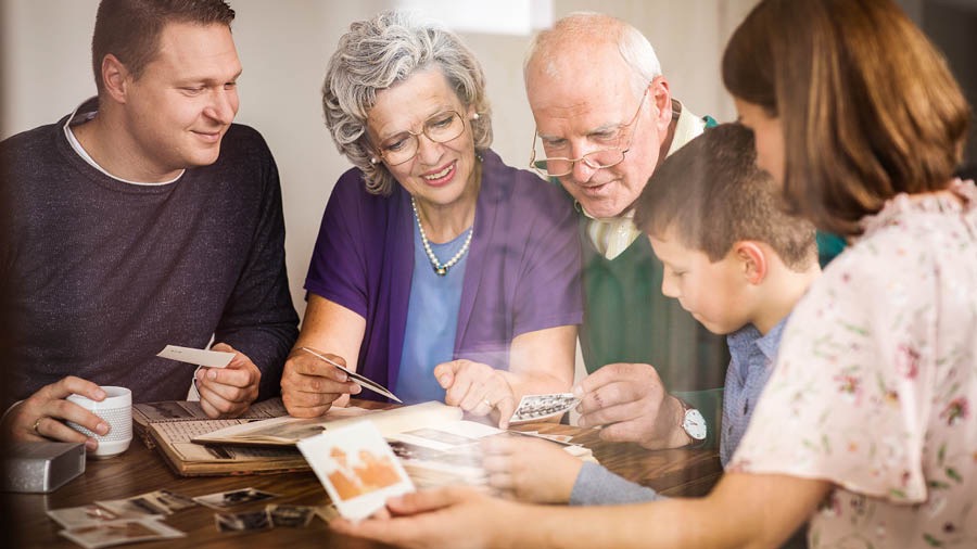 Een echtpaar kijkt samen met hun volwassen dochter en haar gezin naar foto’s terwijl ze herinneringen ophalen aan hun leven in Jehovah’s dienst