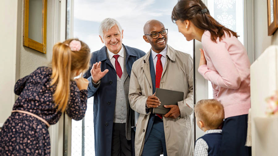 De moeder en haar kinderen verwelkomen twee ouderlingen die op bezoek komen.