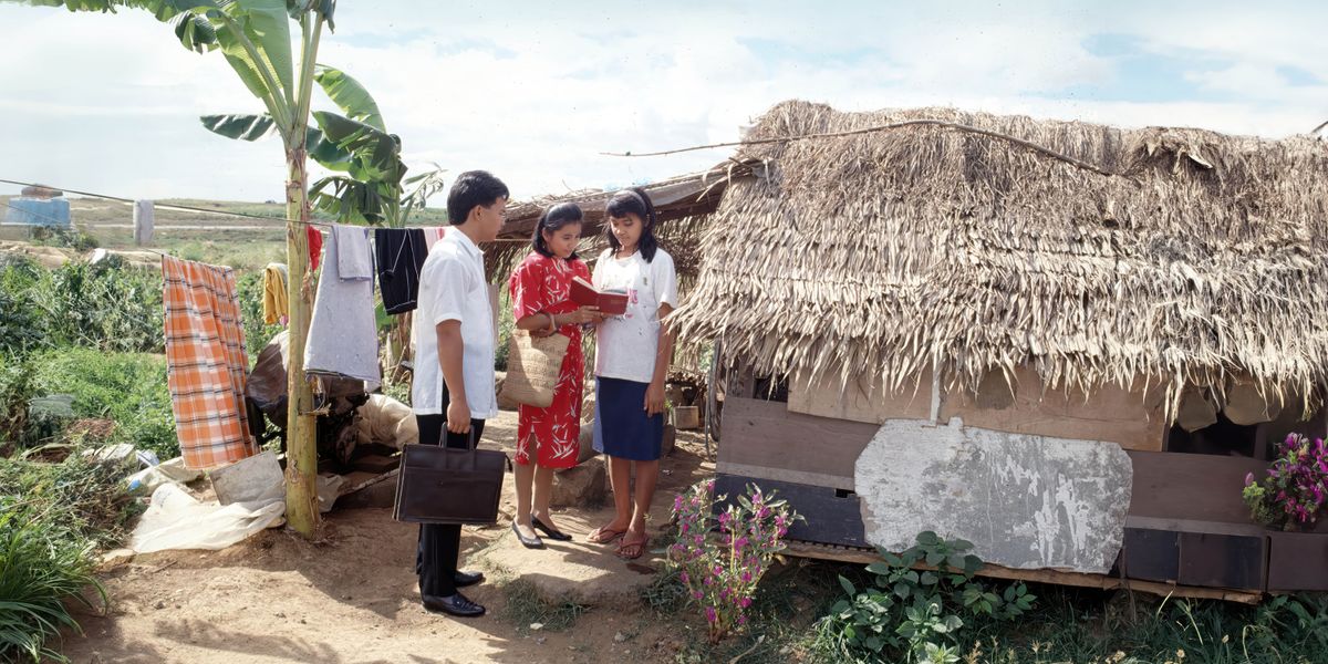 Um casal nas Filipinas dando testemunho para uma mulher do lado de fora da sua casa, que é bem simples.