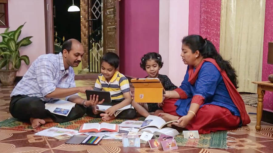 Uma cena do vídeo ‘Construa uma Casa Firme e Forte — Proteja Seus Filhos ‘Quanto ao Que É Mau’.’ Um pai e uma mãe estudando com seus filhos uma parte do livro ‘Aprenda do Grande Instrutor’ e outras publicações.