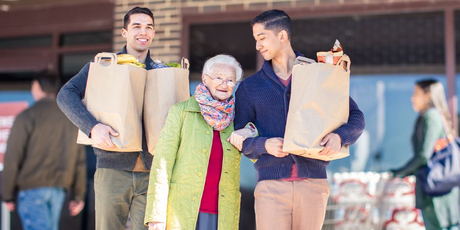 Dois irmãos jovens carregando a sacola de compras de uma irmã idosa