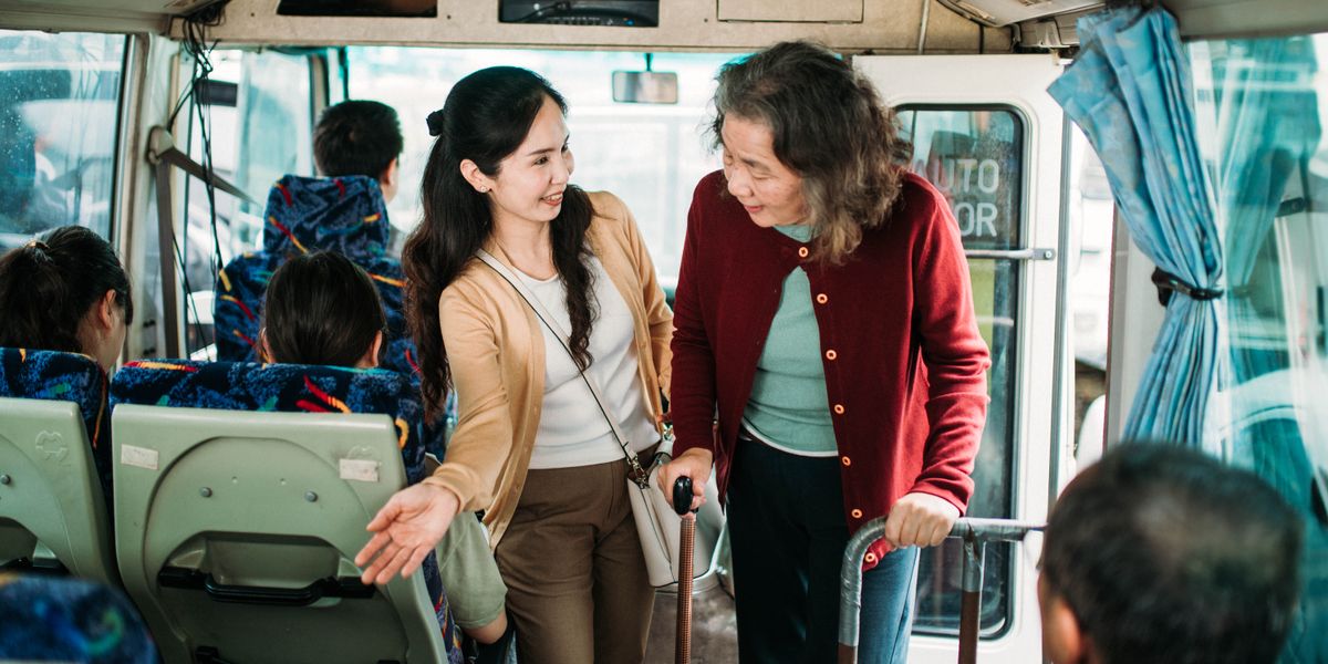 O tânără ajutând-o cu bunătate pe o femeie în vârstă să ajungă la un loc liber din autobuz