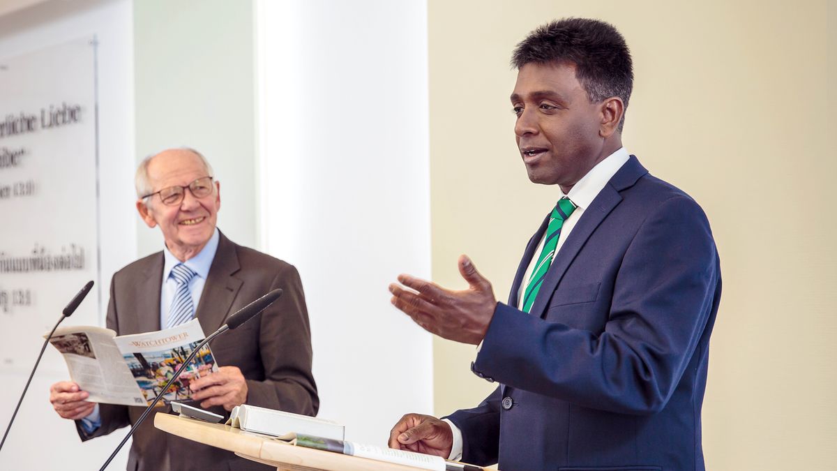 Пожилой брат, который читает на изучении «Сторожевой башни», с одобрительной улыбкой смотрит на более молодого брата, который проводит это изучение.