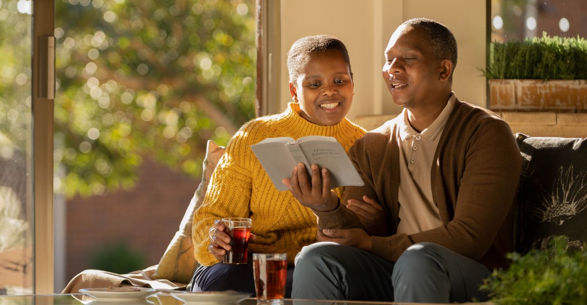 Муж и жена вместе читают Библию, у них на лицах улыбка.