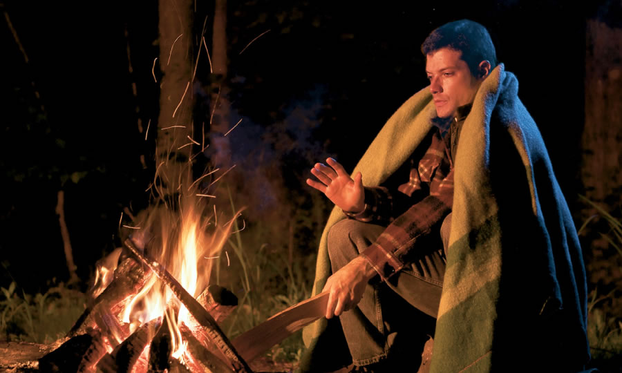 A man getting warm by a fire and adding wood to it