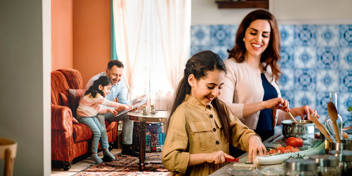 Birlikte zaman geçirmekten mutlu olan bir aile. Anne kızlarından biriyle mutfakta yemek yapıyor. Baba evin diğer kızıyla oturma odasında fotoğraflara bakıyor.