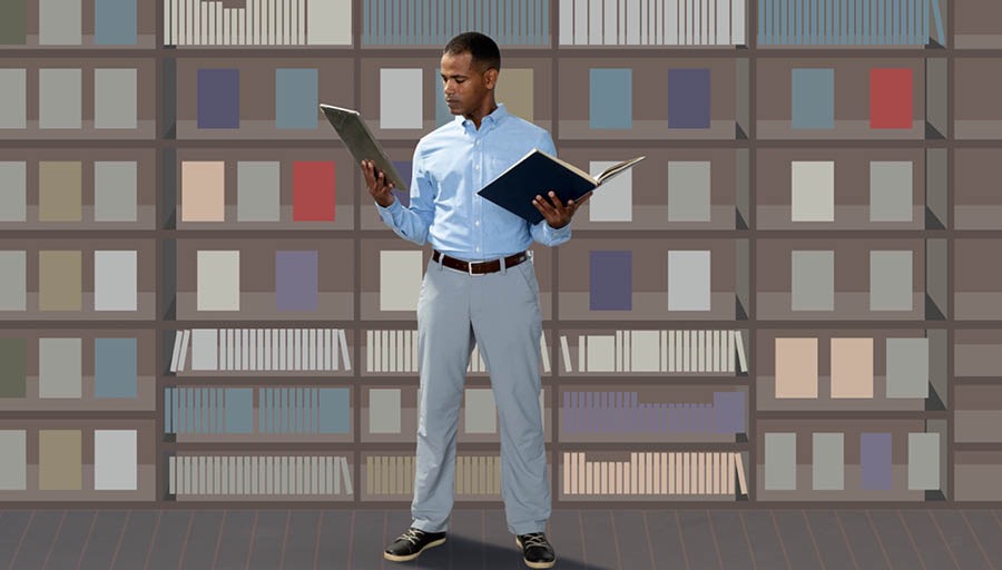 Indoda efanayo ibuka incwadi eyikhethe eshalofini lezincwadi futhi iyiqhathanisa nalokho eye yakuthola emshinini wayo wezobuchwepheshe